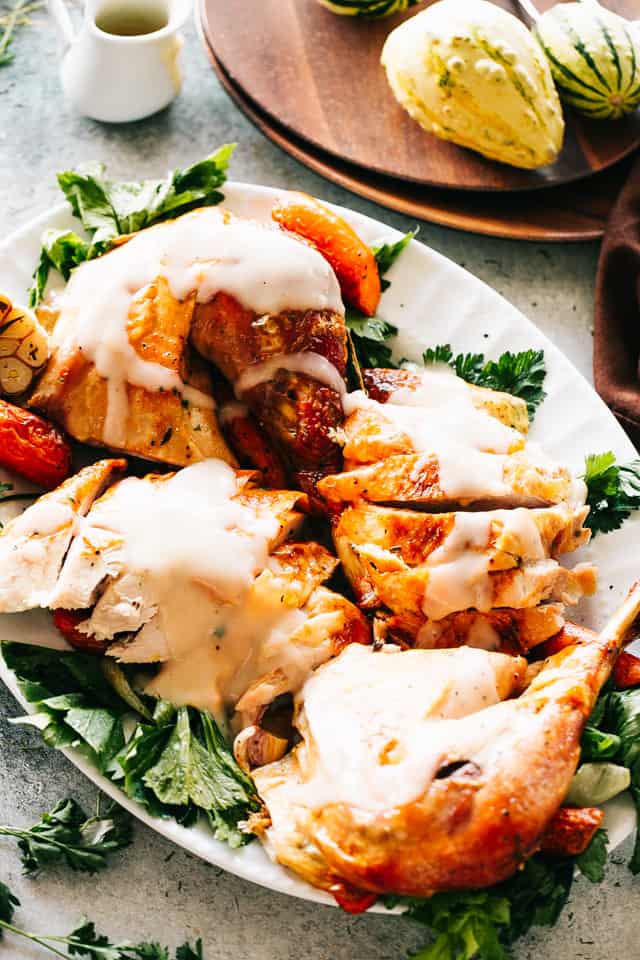 Master how to roast a Thanksgiving turkey with this easy, no-brine method. Cook tender, juicy roast turkey topped with homemade turkey gravy! Carved Thanksgiving turkey served over a bed of greens on a platter, topped with maple turkey gravy.