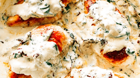 Four creamy Tuscan chicken breasts in a pan.