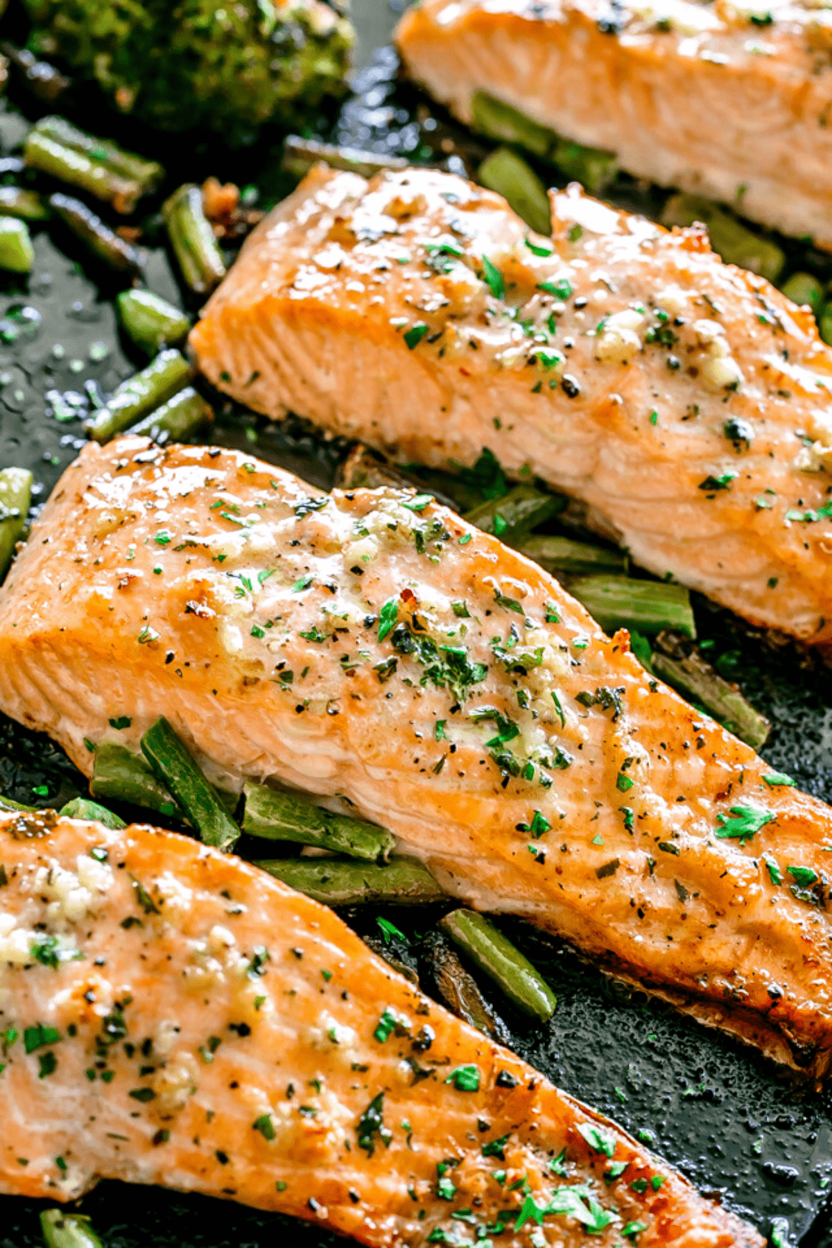 Seasoned salmon fillets baked on a sheet pan over a bed of green vegetables.