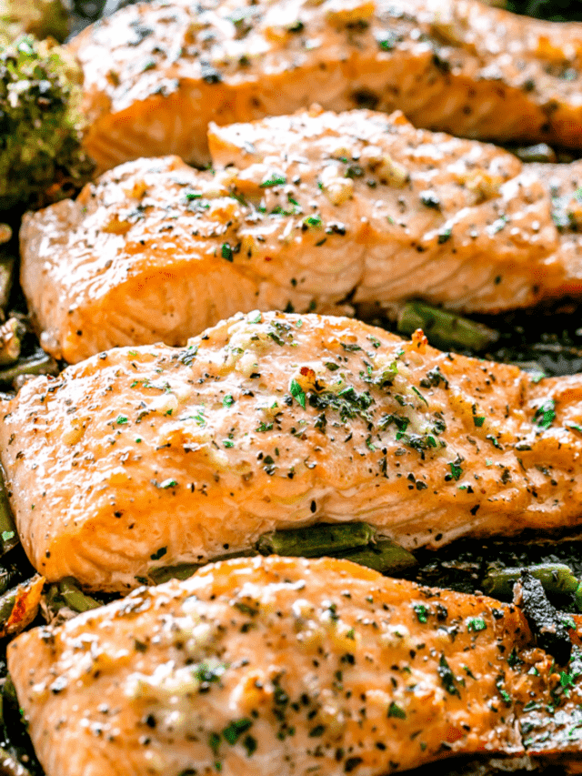 overhead shot of four baked salmon fillets on a sheet pan set on top of green vegetables.