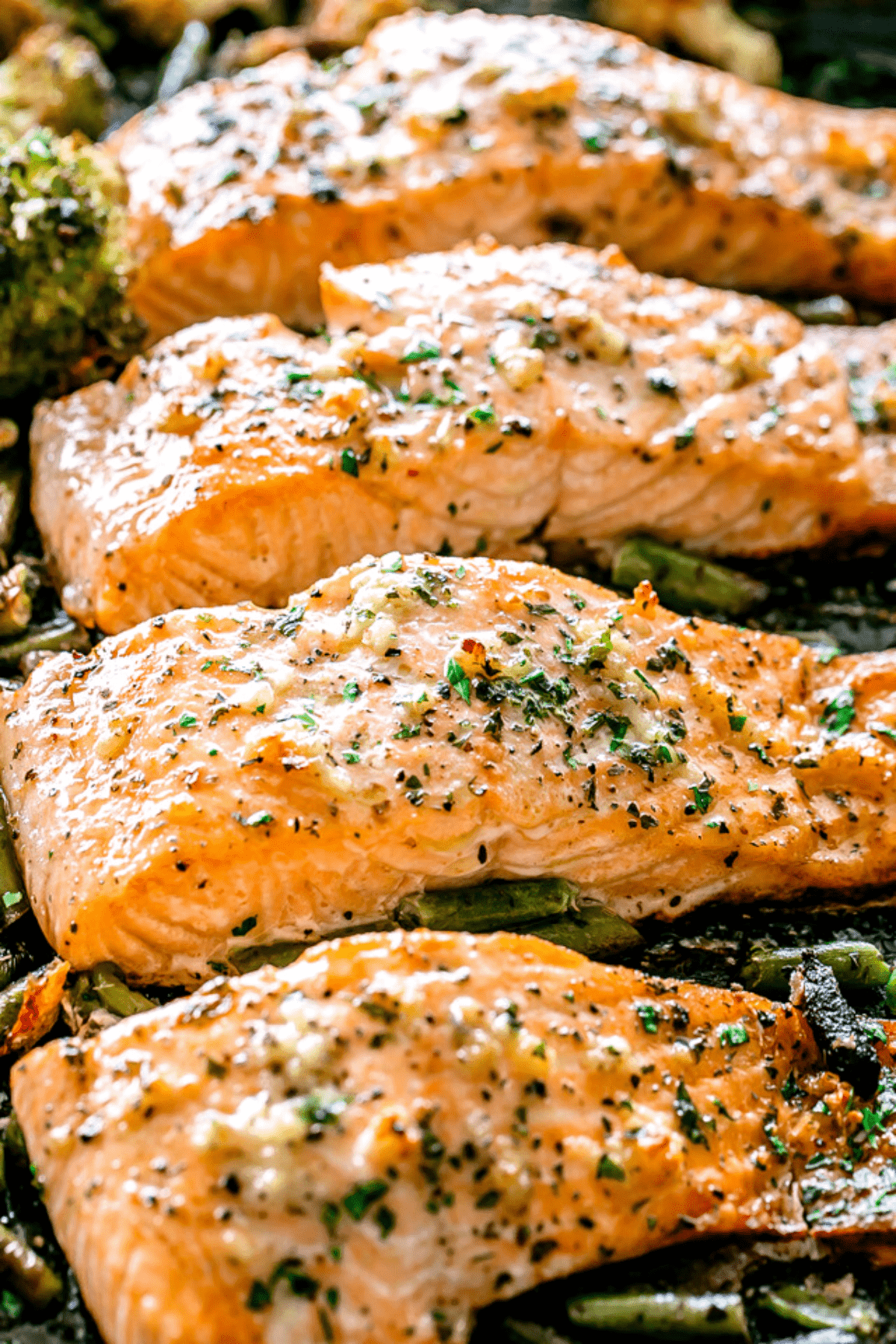 overhead shot of four baked salmon fillets on a sheet pan set on top of green vegetables.