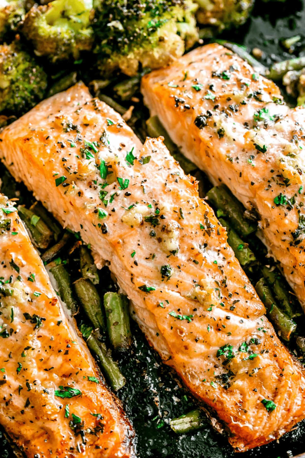 overhead shot of three baked salmon fillets on a sheet pan set on top of green vegetables.
