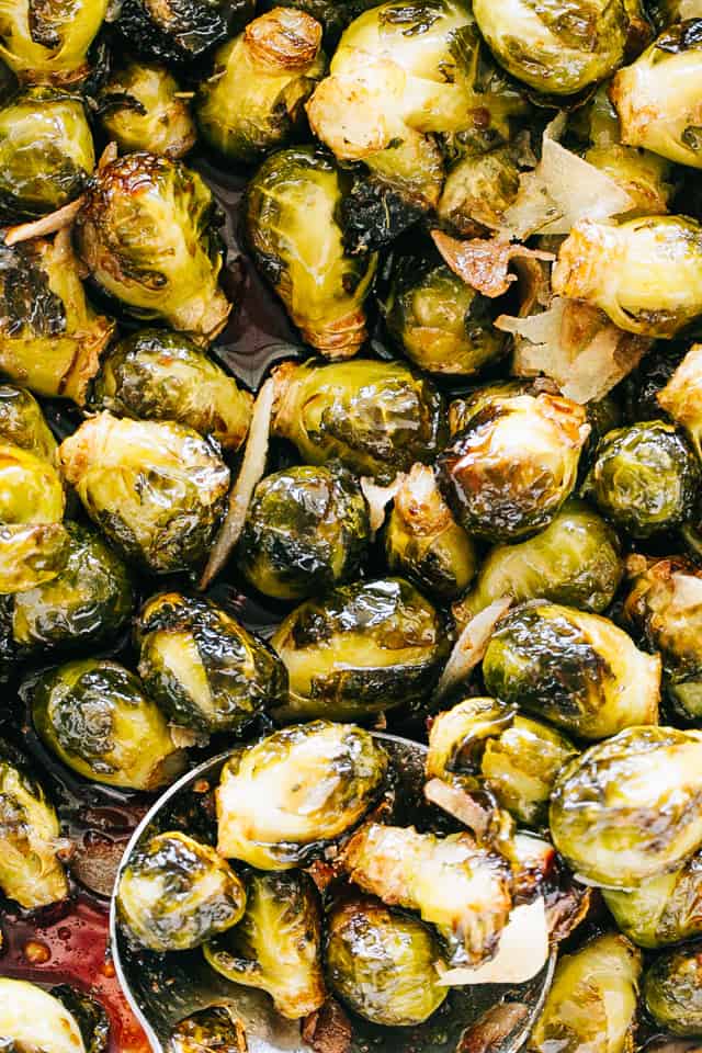 Oven roasted Brussels sprouts in a white ceramic roasting pan with a large spoon for serving.