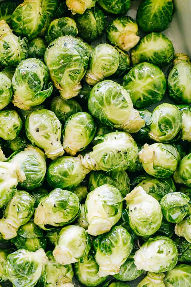 Close up view of raw Brussels sprouts in a white ceramic roasting pan.