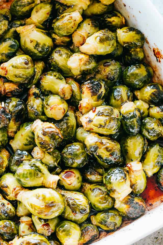 Overhead view of oven roasted Brussels sprouts in a white ceramic roasting pan.