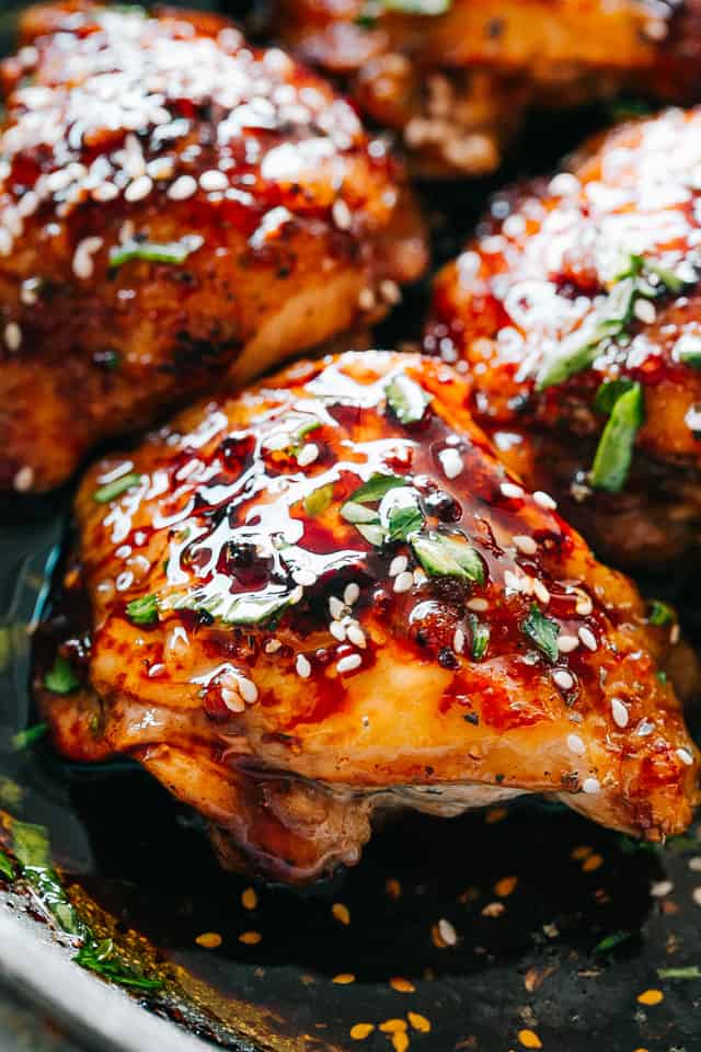 Close-up photo of cooked chicken thighs topped with a sticky sauce, sesame seeds, and a garnish of chopped cilantro.