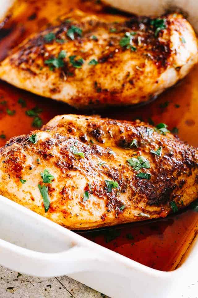 Baked seasoned chicken in a white baking dish.