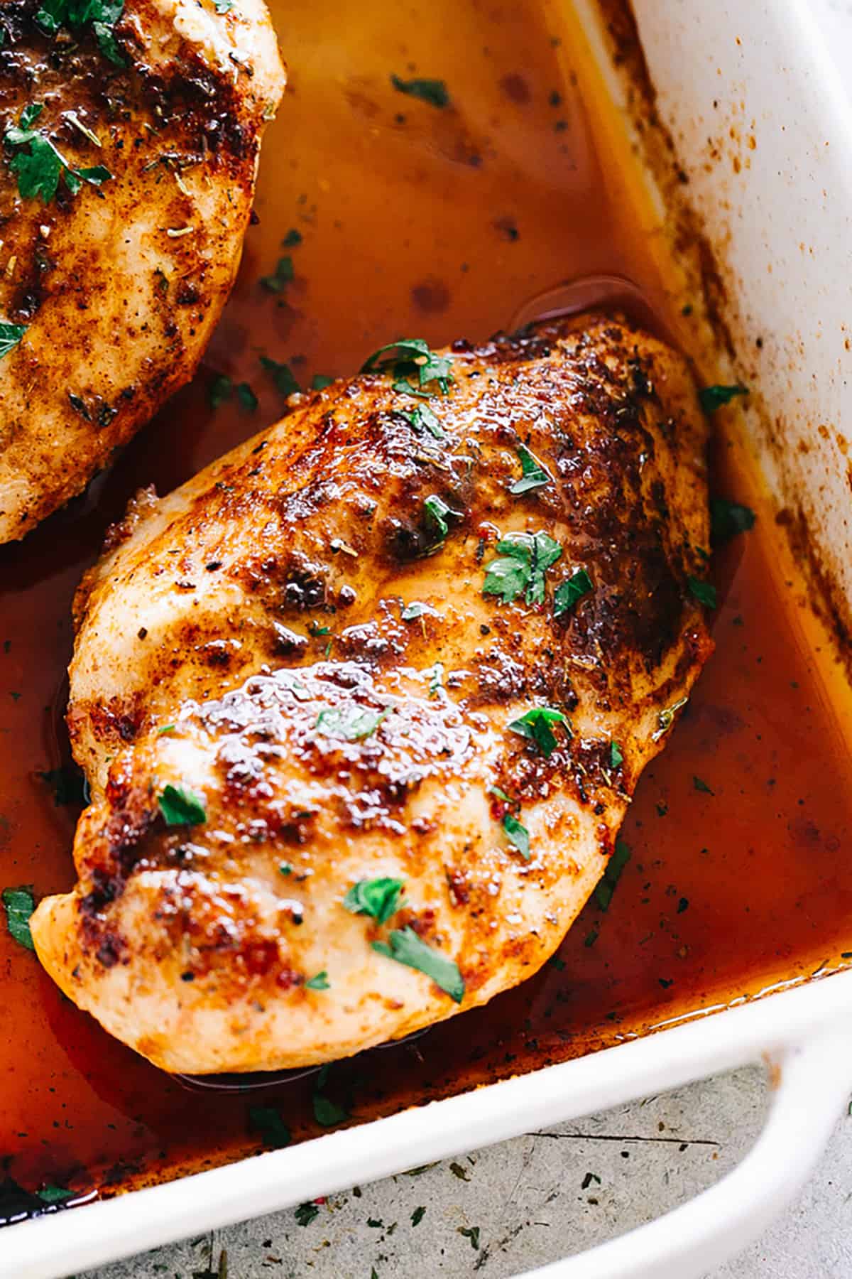 two roasted chicken breasts in a white square baking dish.