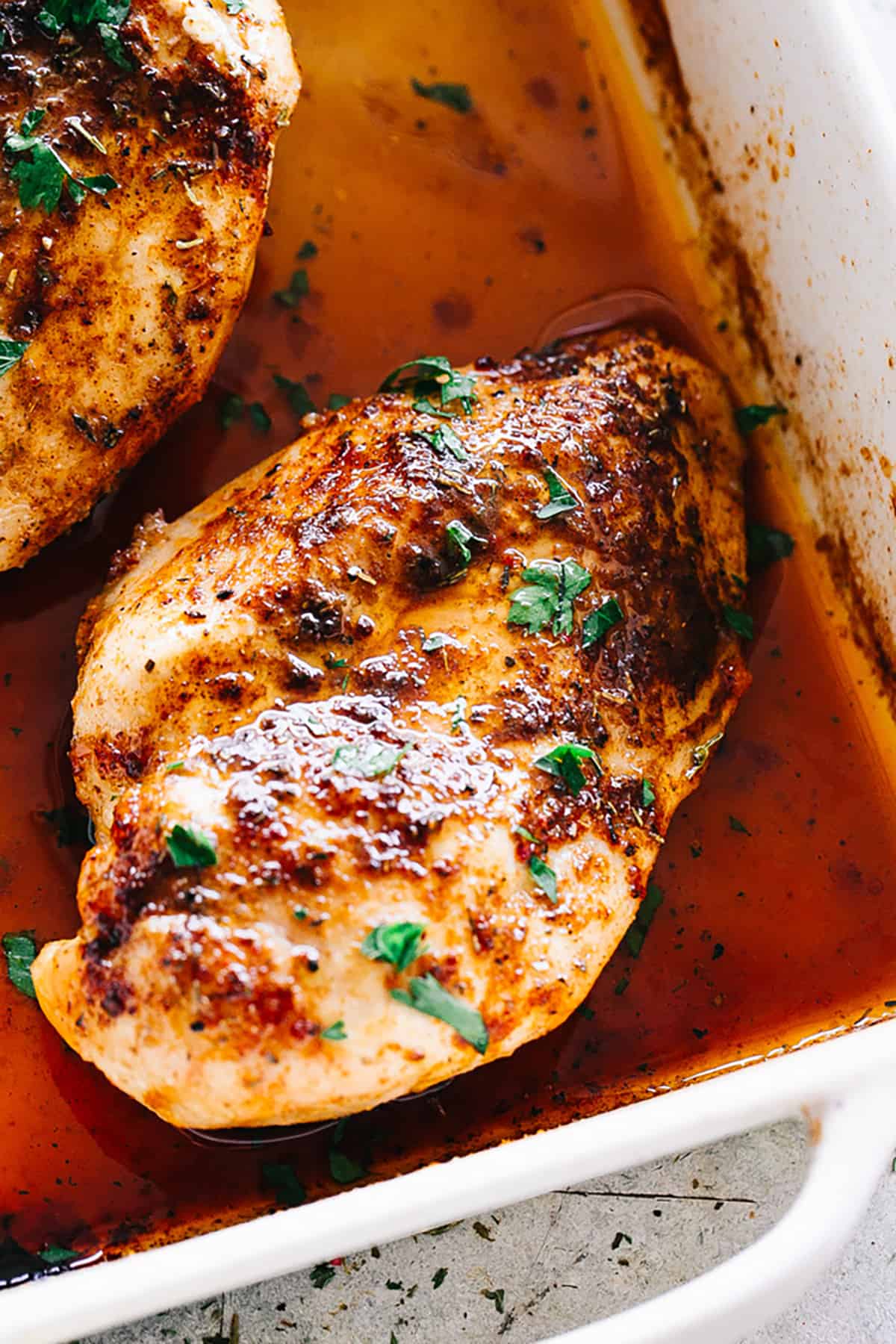 two baked chicken breasts in a white square baking dish.