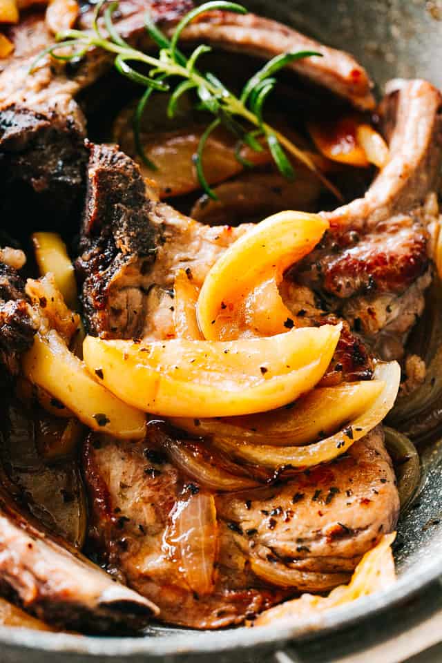 A skillet full of pork, apples and onion being cooked with herbs in apple cider and olive oil.