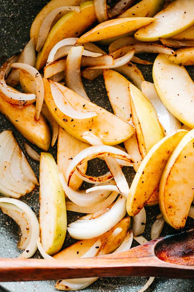 Apple slices and strips of onion being sauteed together over the stove.