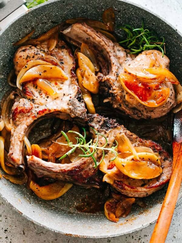 Three Skillet Pork Chops with apples, onions, and fresh herbs in a pan.