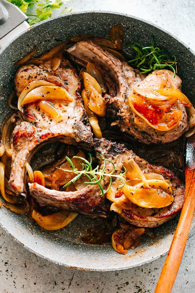 Three Skillet Pork Chops with apples, onions, and fresh herbs in a pan.