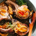 Three pork chops in a skillet with sauteed apple and onion slices piled on top.