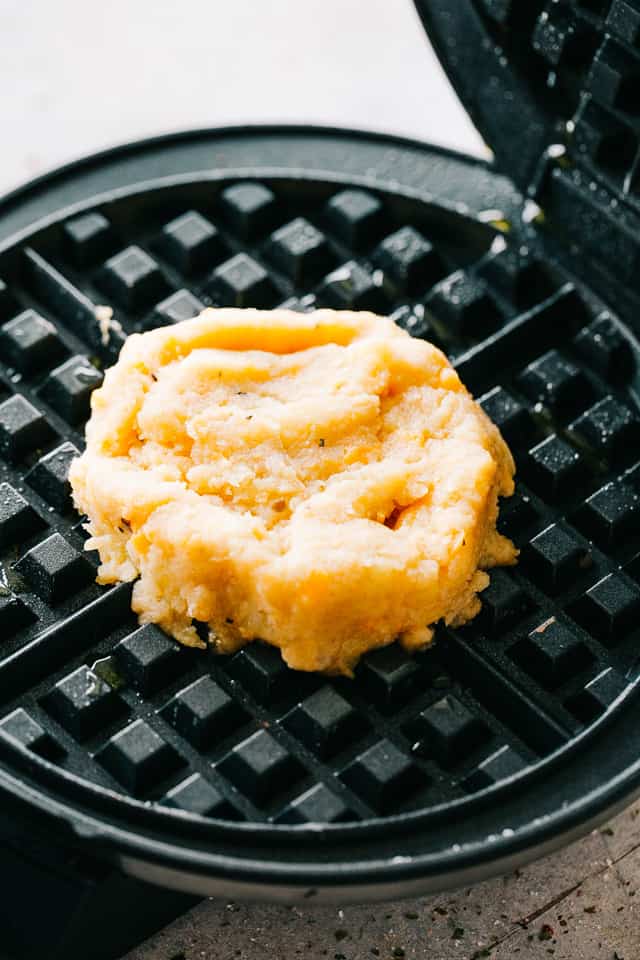 Batter of mashed potatoes cooking in a waffle maker.