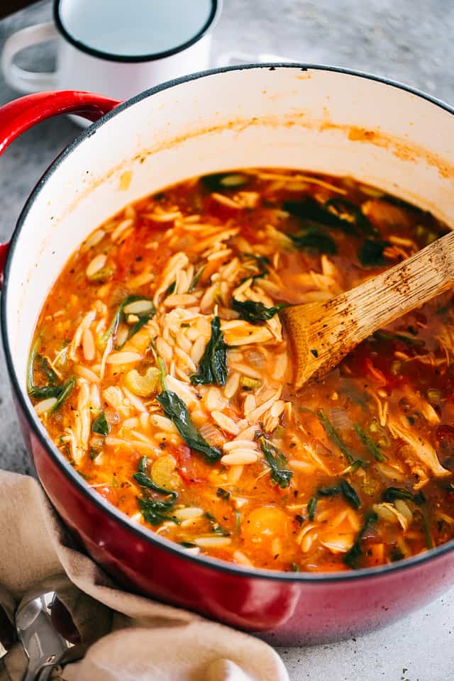 A pot of leftover turkey orzo soup with spinach, with a wooden spoon.