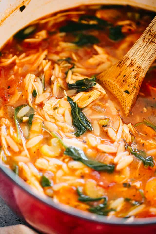 A pot of leftover turkey orzo soup with spinach, with a wooden spoon.