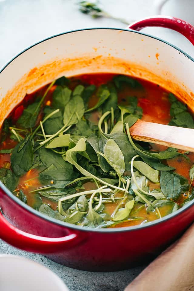 Spinach leaves are added into a pot of turkey soup.
