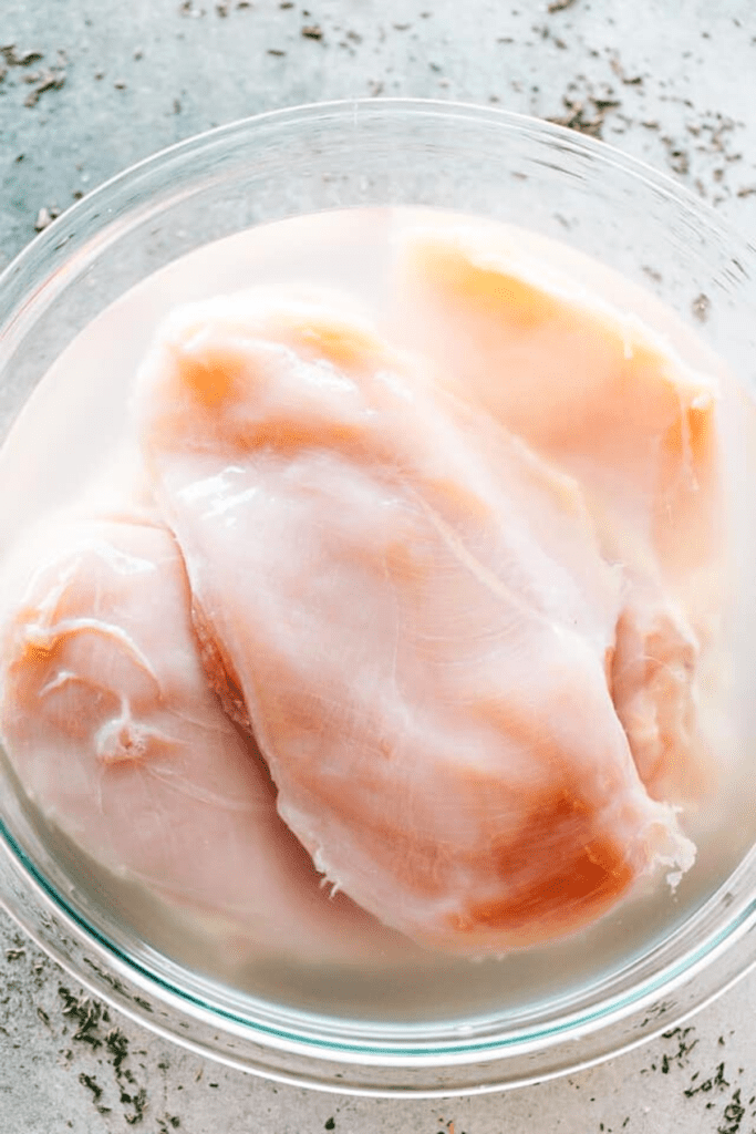 four raw chicken breasts in salt and water brine.