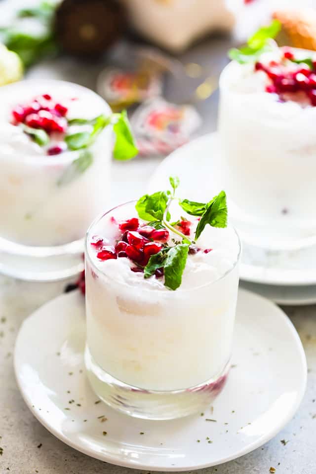 Coconut mojitos served in a whisky glass and garnished with pomegranate seeds and fresh mint leaves.