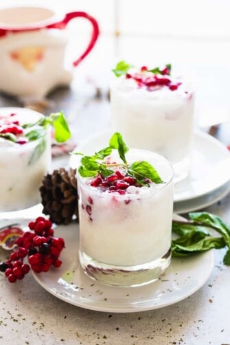 Several coconut mojitos served in a whisky glass and garnished with pomegranate seeds and fresh mint leaves.