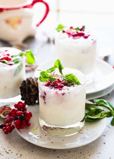Several coconut mojitos served in a whisky glass and garnished with pomegranate seeds and fresh mint leaves.