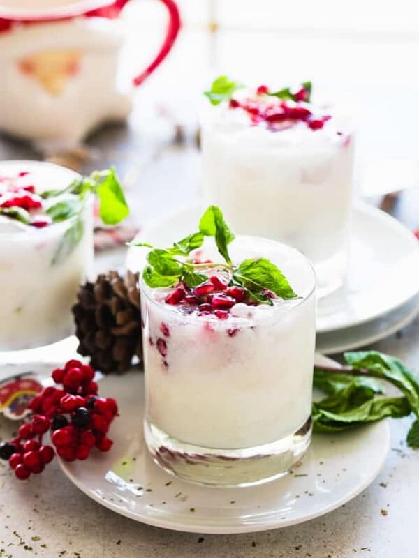 Several coconut mojitos served in a whisky glass and garnished with pomegranate seeds and fresh mint leaves.