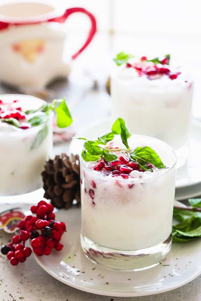 Coconut mojitos served in a whisky glass and garnished with pomegranate seeds and fresh mint leaves.