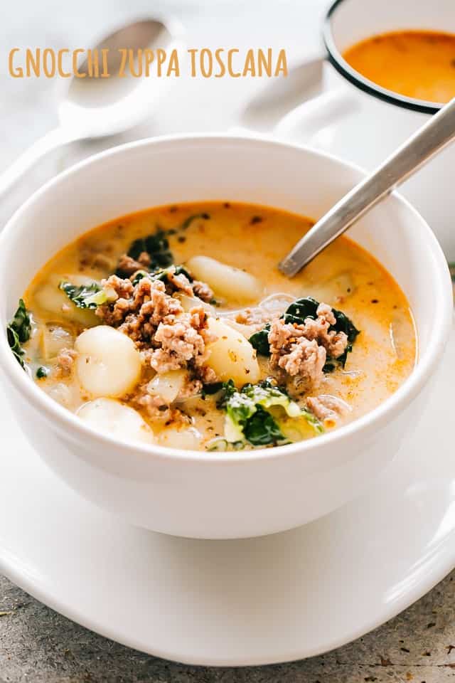 A white bowl filled with creamy zuppa toscana soup filled with gnocchi, Italian sausage, and kale.