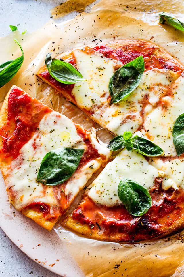 Keto Pizza Margherita Recipe set on pizza wheel, cut into 4 slices, and topped with fresh basil leaves