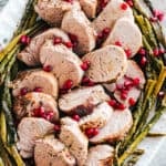 An oval-shaped platter filled with roasted pork tenderloin and roasted asparagus