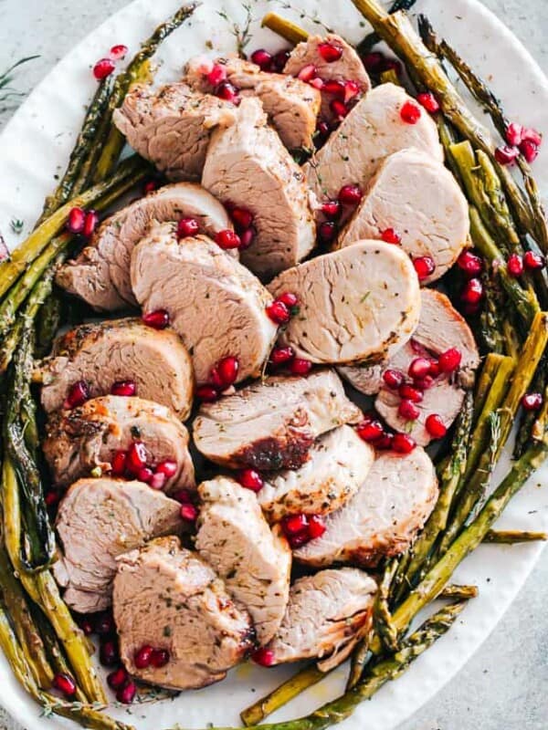 An oval-shaped platter filled with roasted pork tenderloin and roasted asparagus