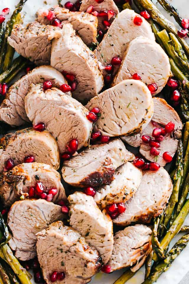 Slices of roasted pork on a large serving platter with roasted asparagus around the edge