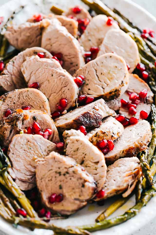 Roasted pork on a large serving platter along with roasted asparagus, pomegranate seeds and chopped fresh thyme