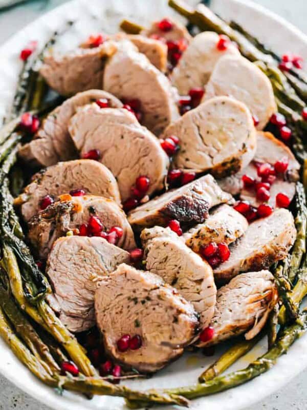 A pile of roasted pork tenderloin slices surrounded by roasted asparagus spears on a platter