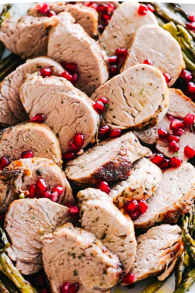 Sliced pork on a serving platter with chopped thyme and pomegranate seeds on top