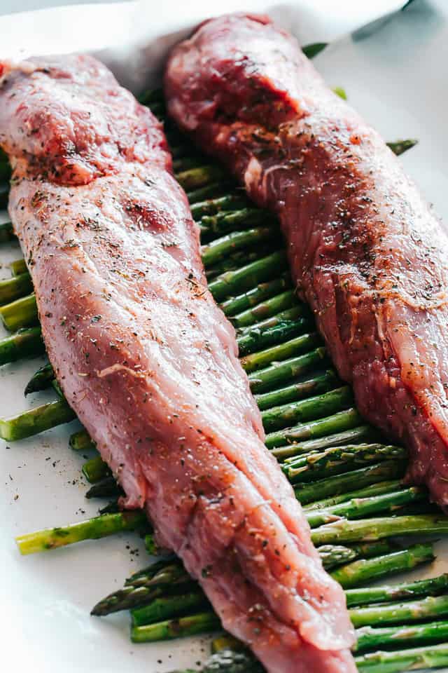 Two seared tenderloins on top of a line of seasoned asparagus spears