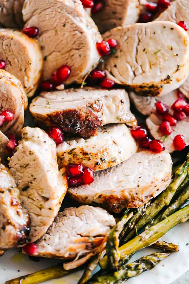 A close-up shot of slices of roasted pork tenderloin with pomegranate seeds on top