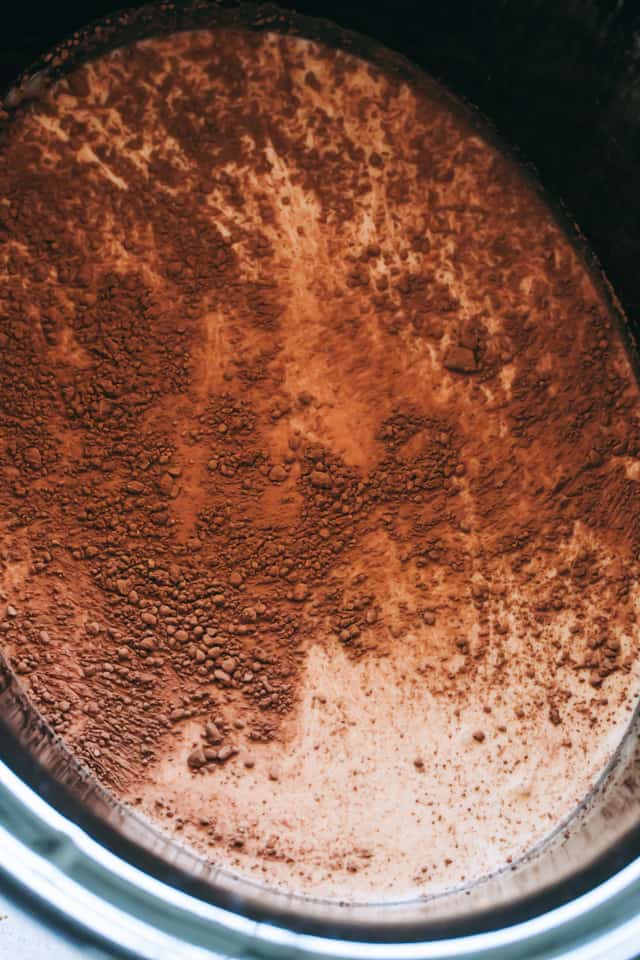 Adding the cocoa powder to the mixture in the crock pot. 
