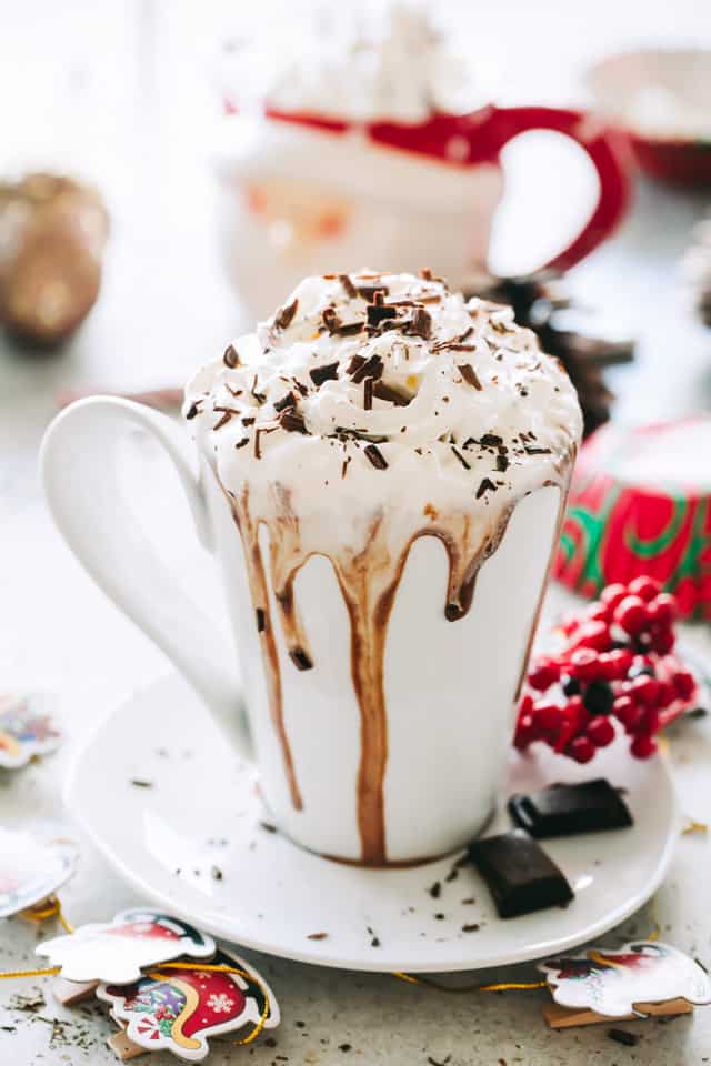 A cup of crock pot hot chocolate with whipped cream and chocolate shavings on top.