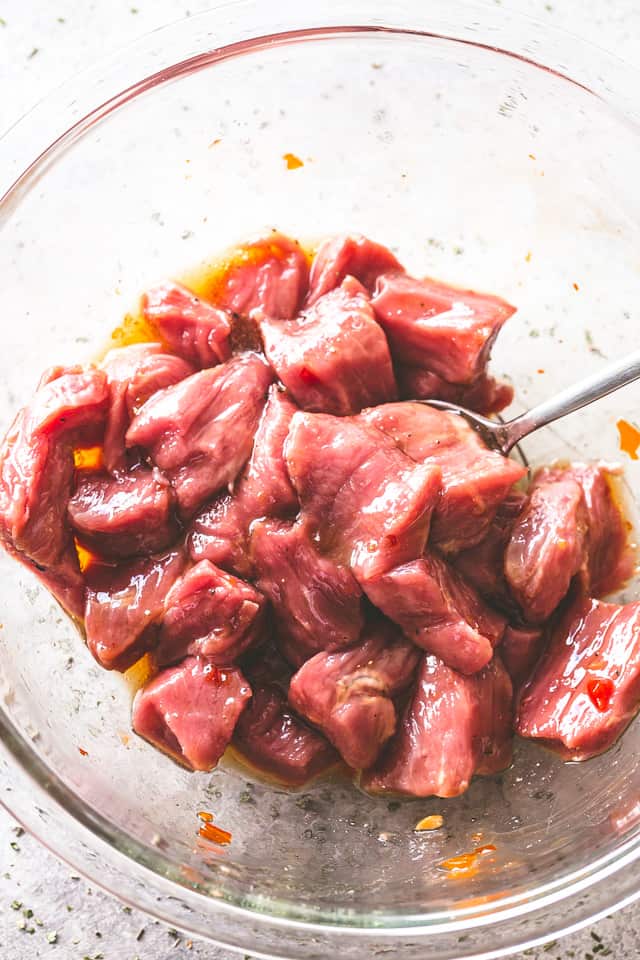 Tossing raw cubed steak in a mixing bowl with chili sauce and honey.