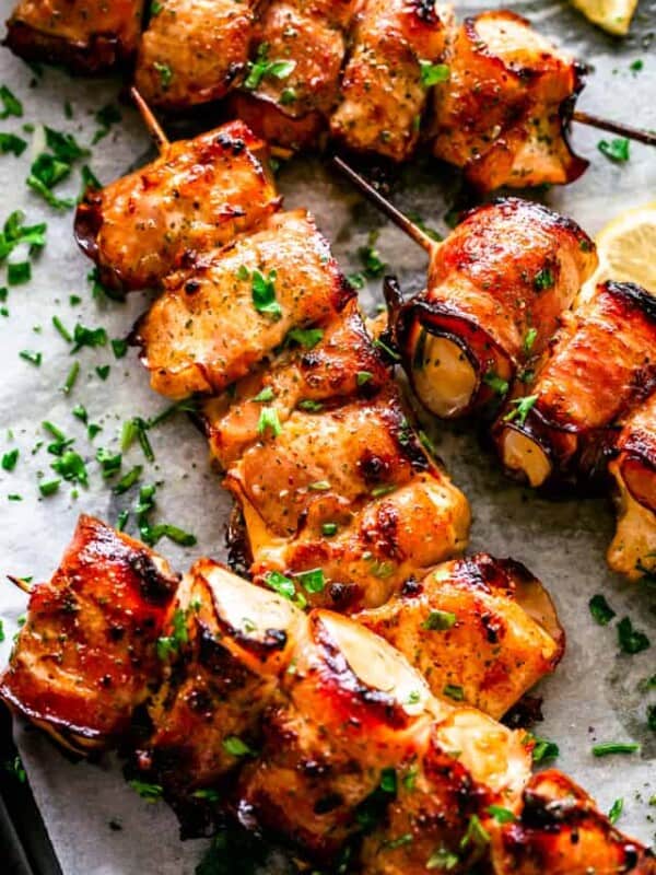 Overhead view of grilled bacon-wrapped chicken bites on skewers garnished with parsley.