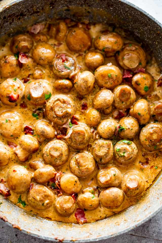 Creamy button mushrooms side dish cooking in a gray skillet.