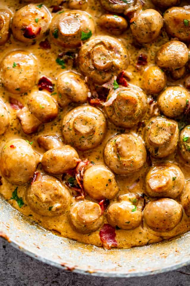 Close-up shot of Garlic Mushrooms with chopped bacon in a skillet.