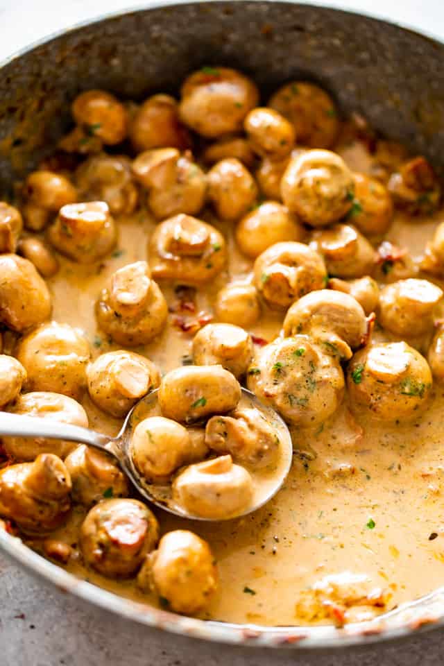 A photo of a skillet with Creamy Garlic Mushrooms and a spoon scooping up the mushrooms.
