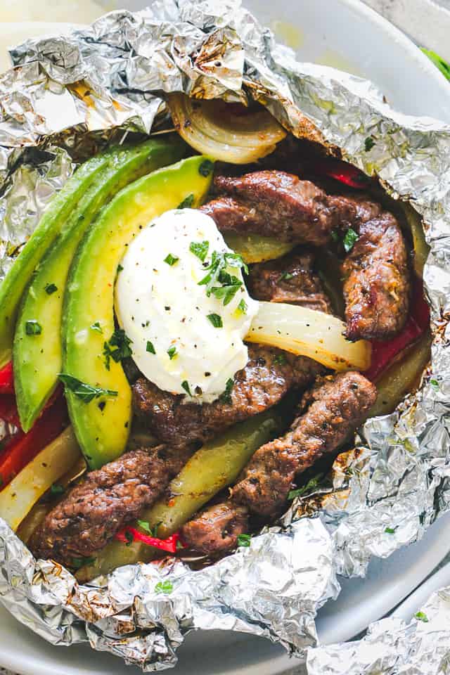 Chili Lime Steak Fajitas in Foil Packs topped with dollop of sour cream, slices of avocado, onions, and bell peppers.