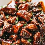 Close-up image of Honey Garlic Steak Bites garnished with sesame seeds and greens, and served in a bowl.