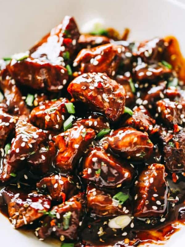 Close-up image of Honey Garlic Steak Bites garnished with sesame seeds and greens, and served in a bowl.