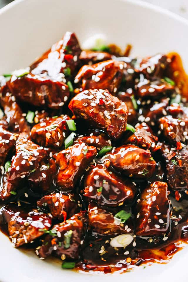 Close-up image of Honey Garlic Steak Bites garnished with sesame seeds and greens, and served in a bowl.