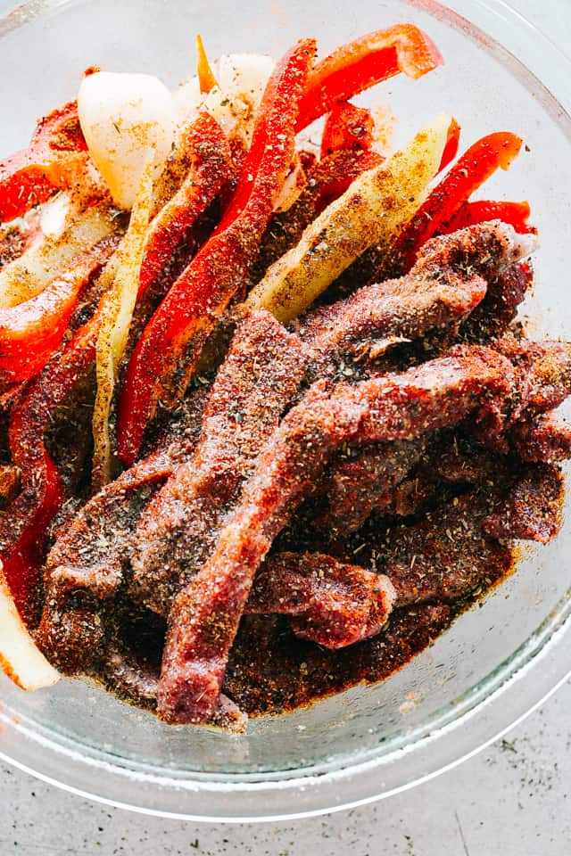 A bowl with sliced flank steak, bell peppers, and onions tossed with fajitas seasoning mix.